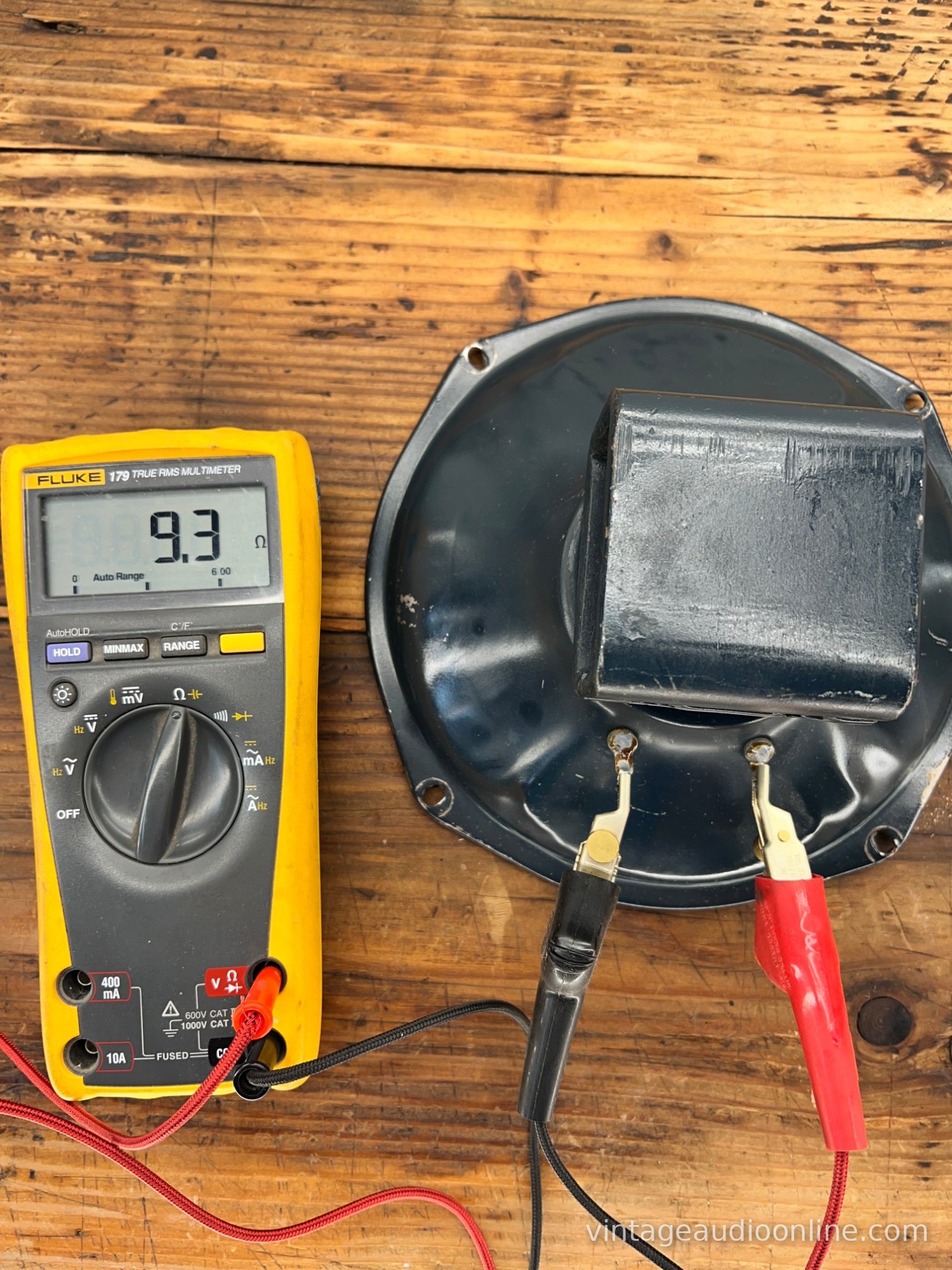 Older speaker driver with a square magnet cover connected to a multimeter